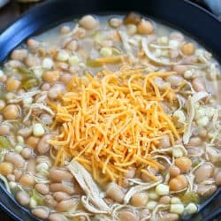 Black bowl filled with white chicken chili and topped with shredded cheese.