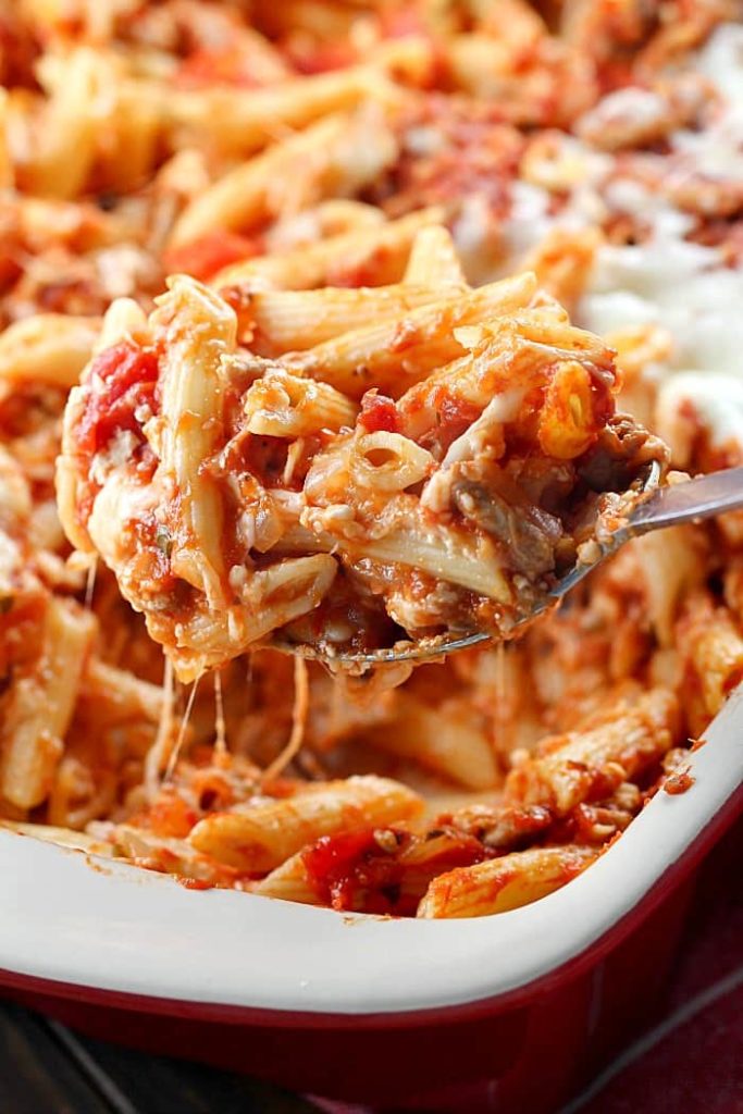 A scoop of Skinny Cheesy Pasta Bake on a silver spoon from a casserole dish.