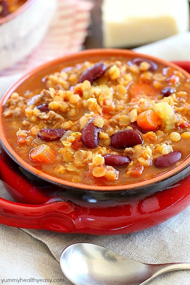 An incredible Sausage Lentil Chili in a red bowl with a spoon in front of it.