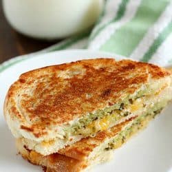 Pesto Grilled Cheese Panini cut in half on a white plate with a glass of milk in the background.