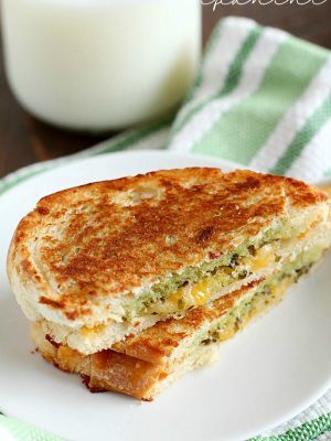 Pesto Grilled Cheese Panini cut in half on a white plate with a glass of milk in the background.