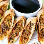 White plate with egg rolls sliced in half, surrounding a bowl of soy sauce.
