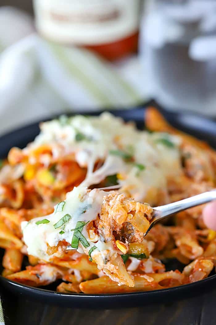 Cheese pull shot of fork full of pasta and roasted summer vegetables.
