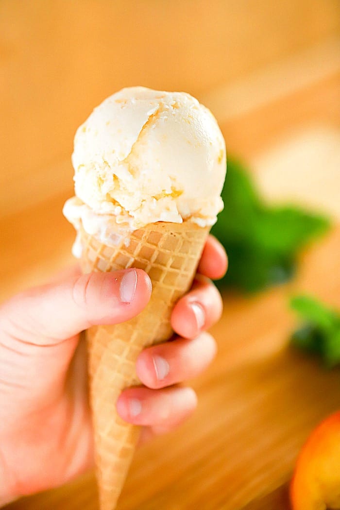 Child's hand holding a waffle ice cream cone filled with peach frozen yogurt.