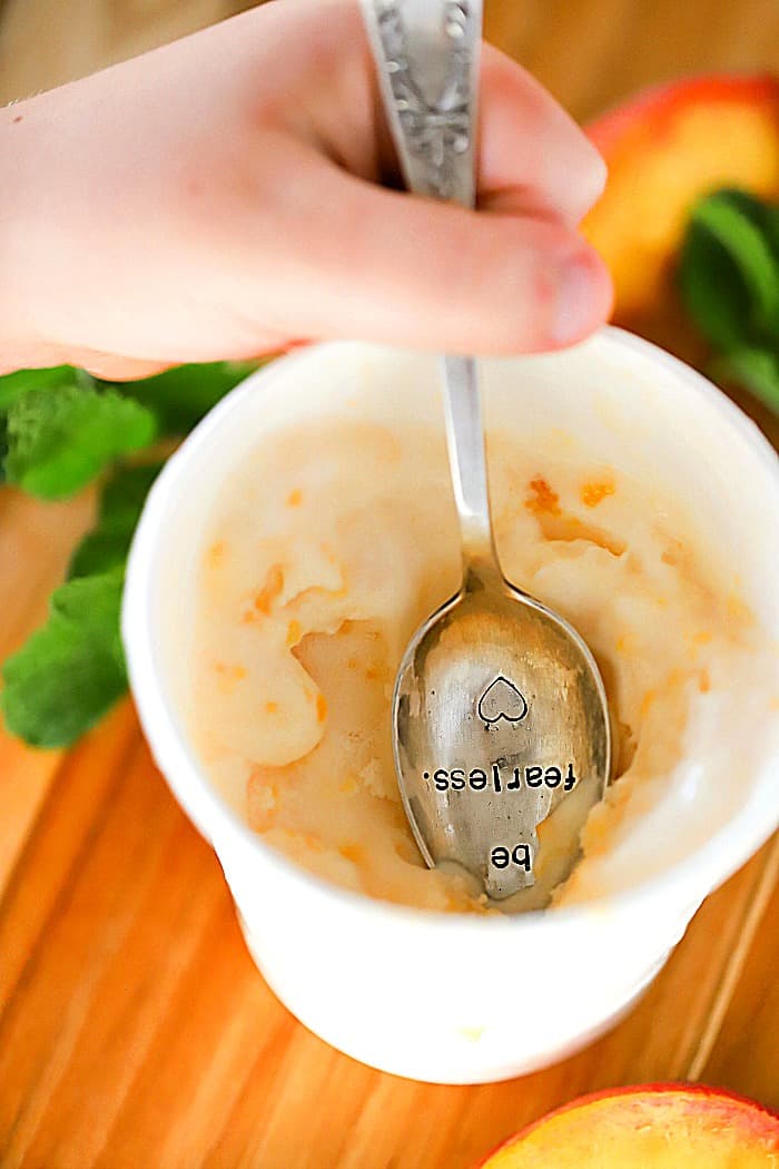A spoon that has "Be Fearless" etched into the spoon is in an ice cream container with frozen yogurt inside it.