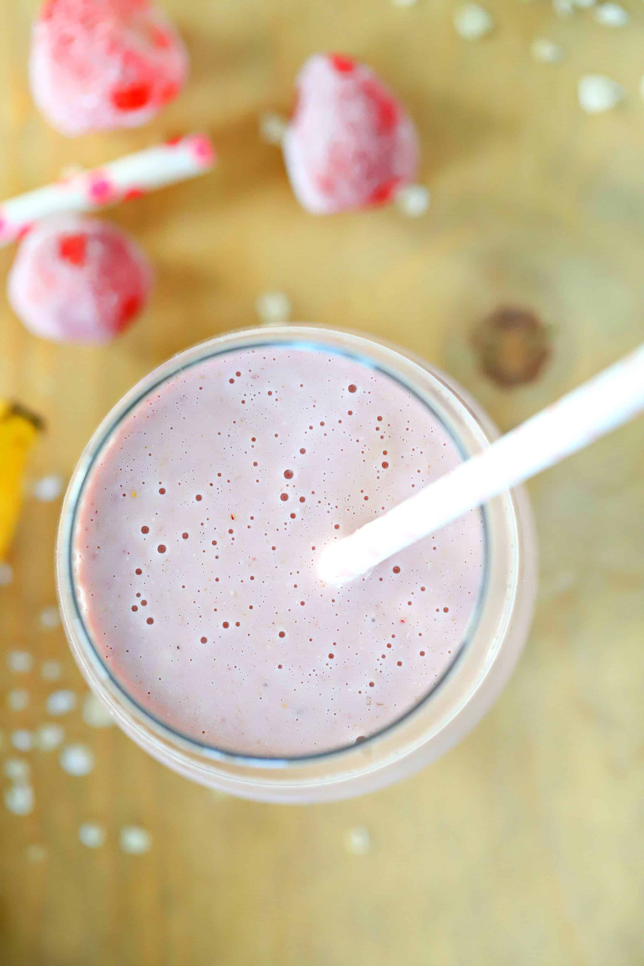 Overhead photo of a strawberry oatmeal smoothie with frozen strawberries in the background