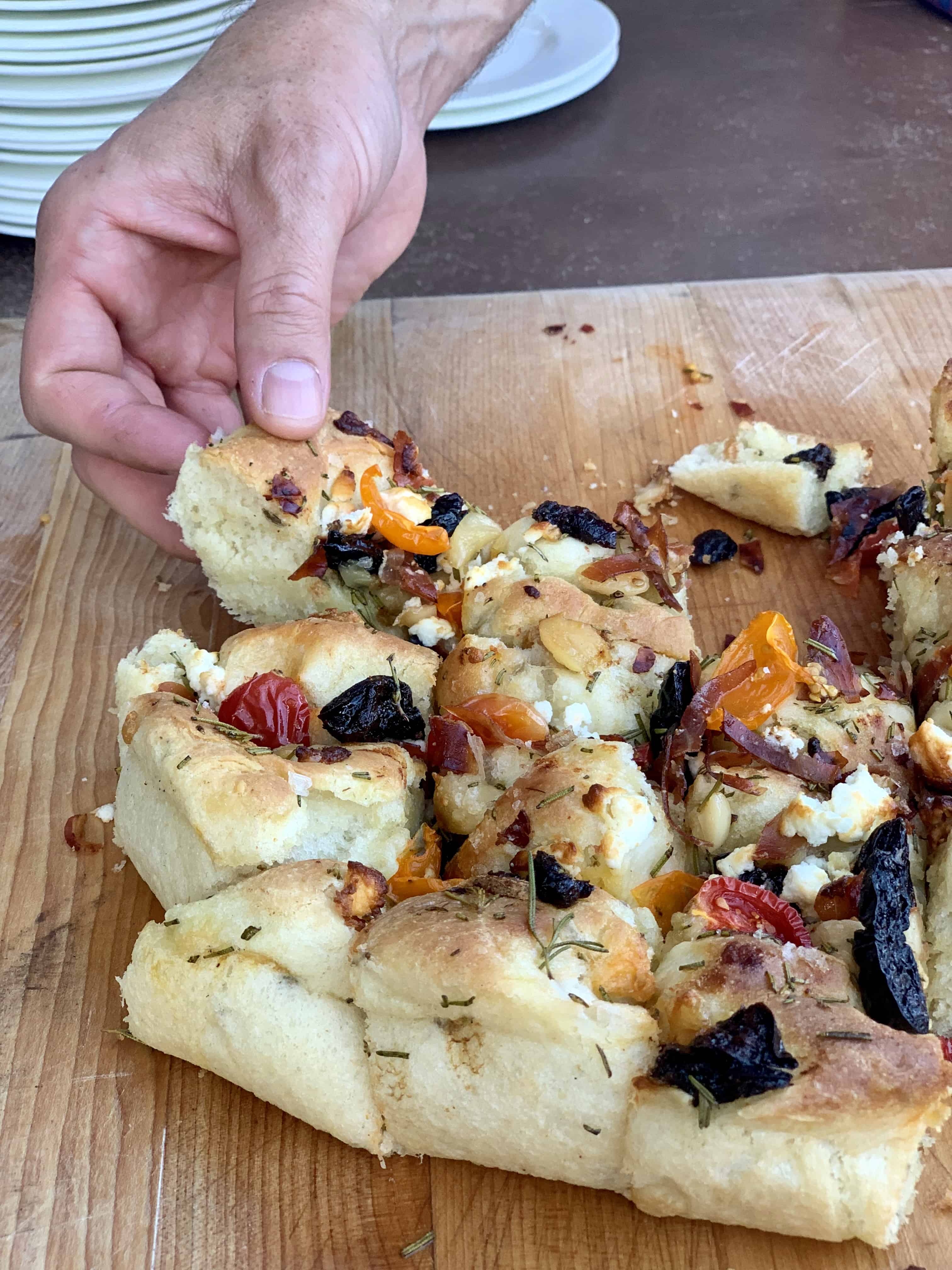 Cast Iron Foccacia Bread with prunes on a cutting board with a cheese pull