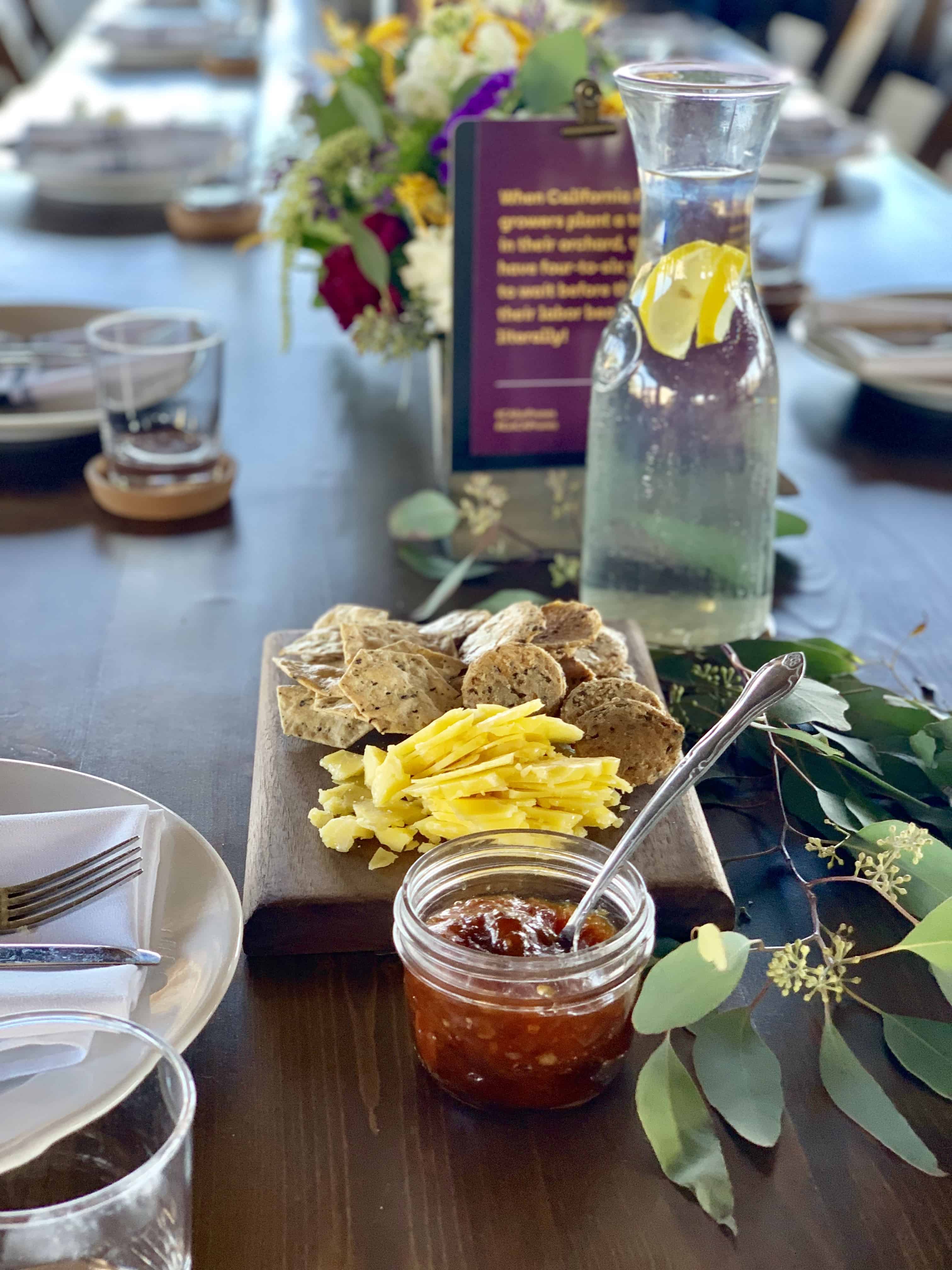 Beautiful tablescape with flowers in the background and cheese, crackers and jam in the foreground.