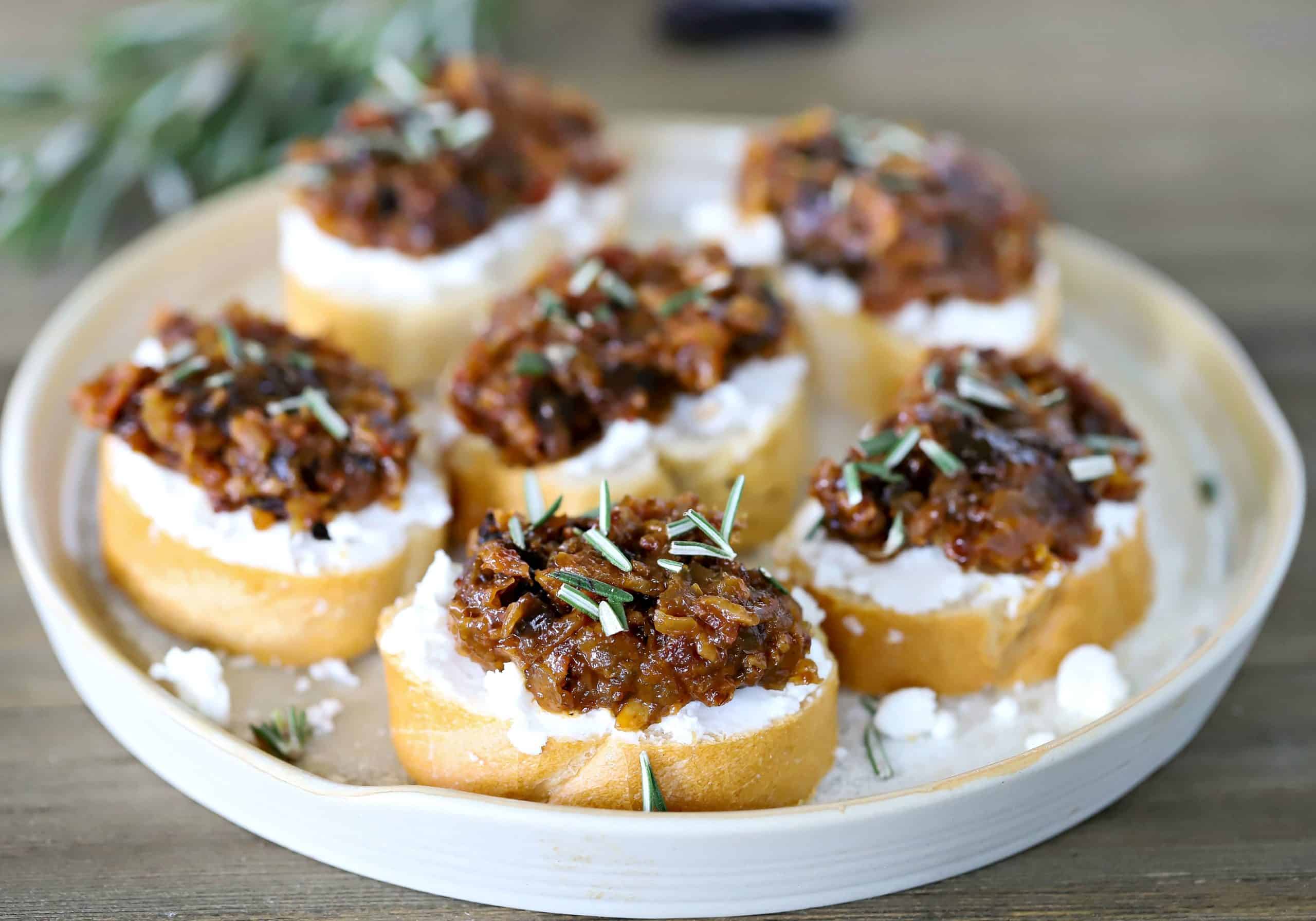 Horizontal white plate full of bacon jam crostini.