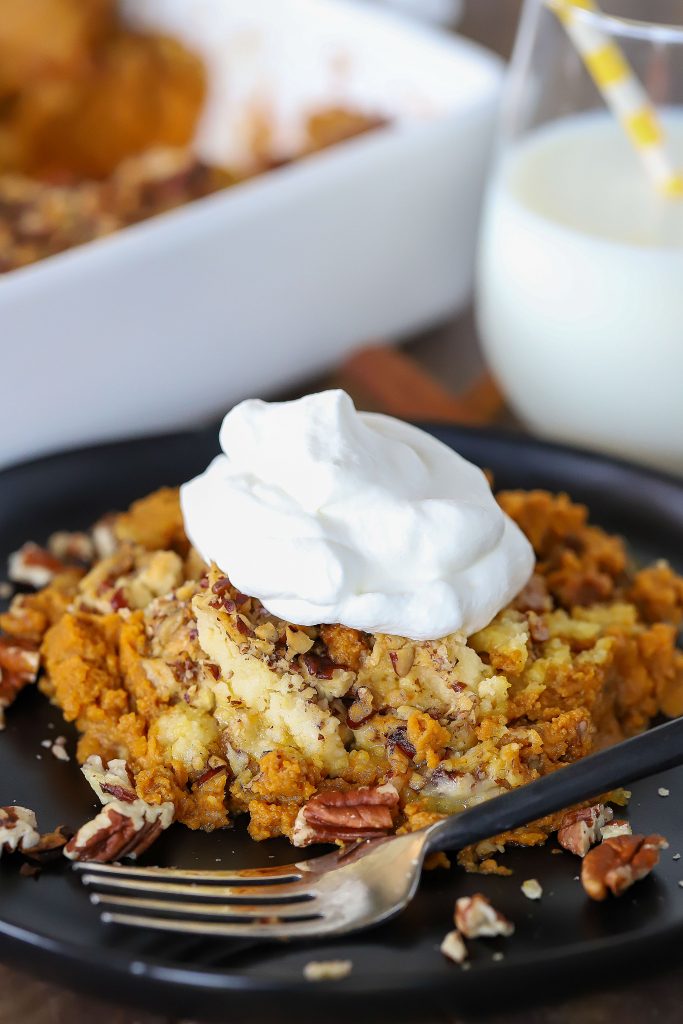 Plate with a piece of Pumpkin Dump Cake and a fork. Plus a glass of milk and casserole dish in the background.