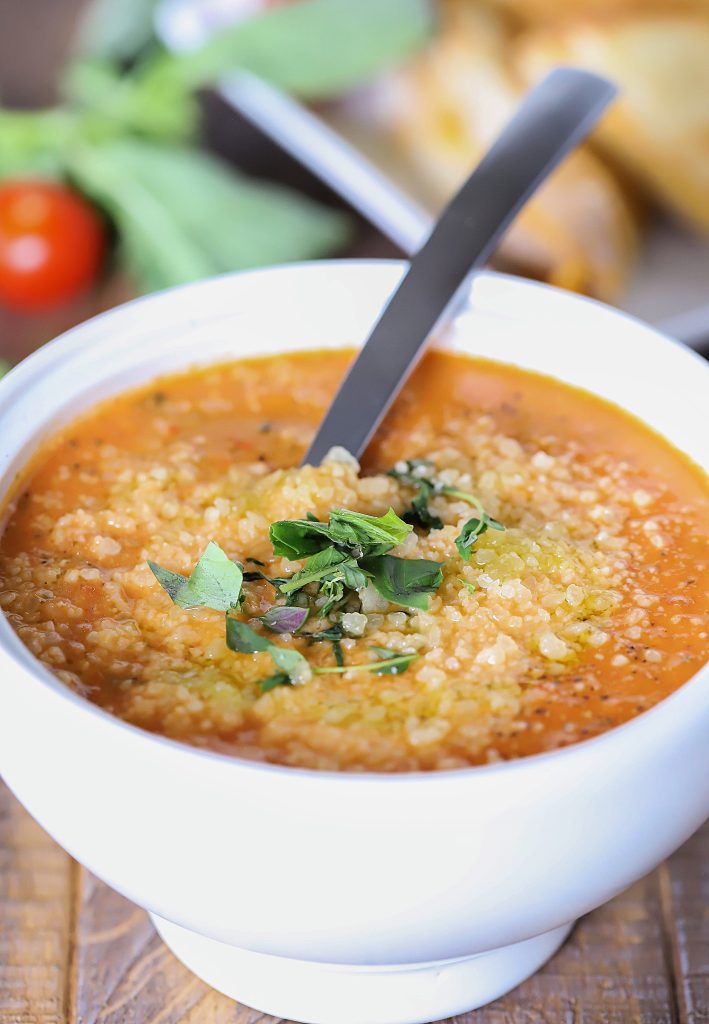 White bowl of tomato soup with parmesan cheese and herbs the top.