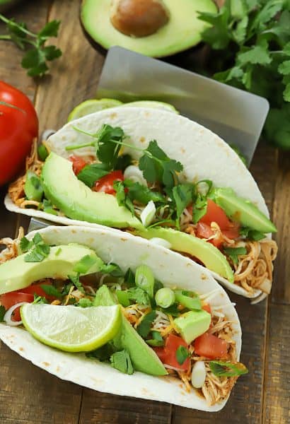 Two taco shells filled with slow cooker taco chicken and topped with avocado, tomato, tomato and green onions.